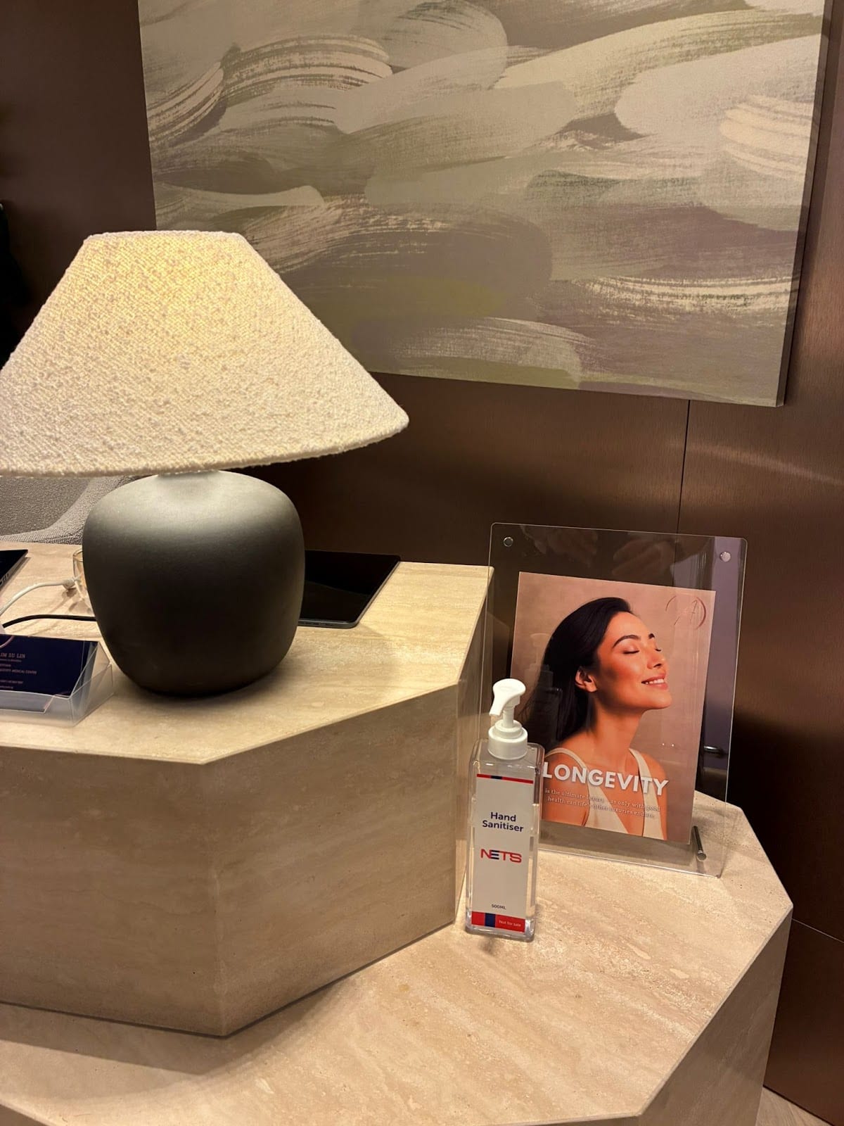 The travertine reception desk at Asia Longevity with a linen table lamp and bronze panelling